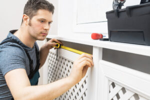 Professional handyman assembling radiator cabinet at home.