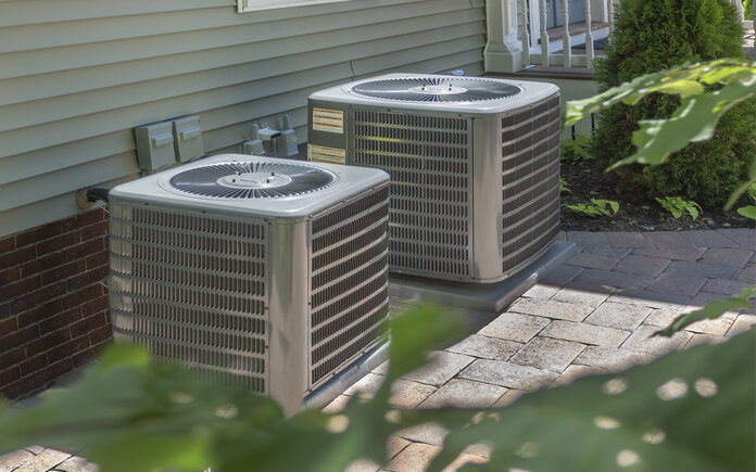 2 steal HVAC systems sitting outside a house, with a tree branch in the front