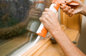 person applying caulk to a window for added insulation