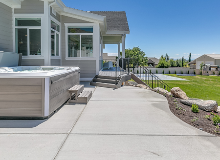 Photo of a concrete patio with a hot tub facing the backyard of a new home